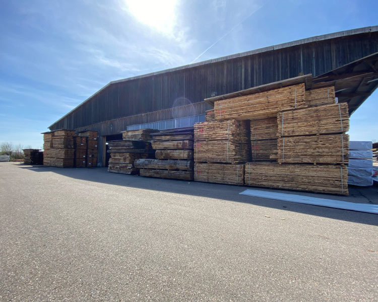 Lagerhalle in Asbach-Bäumenheim mit gestapeltem Holz davor | Massivholzplatten | Burger Holzzentrum